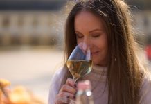 Woman drinking tasting a glass of white wine outdoor, enjoying scenting aroma, smiling