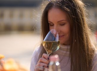 Woman drinking tasting a glass of white wine outdoor, enjoying scenting aroma, smiling