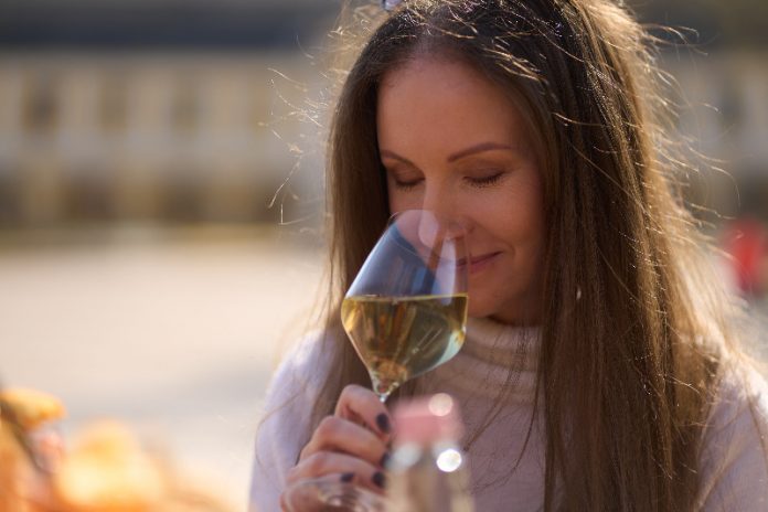 Woman drinking tasting a glass of white wine outdoor, enjoying scenting aroma, smiling