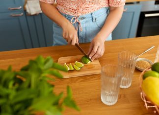 close up of woman cutting lime with knife and making mocktail at home kitchen