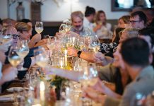Traverse City Food & Wine Festival: Looking Back on Its Inaugural 2025 and Forward to 2026 A group of people sitting at a table and raising their wine glasses for a toast.